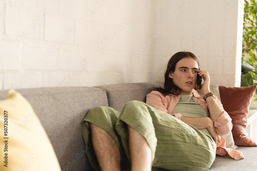 Non-binary trans woman talking on smartphone lying on the couch at home Non-binary trans woman talking on smartphone lying on the couch at home