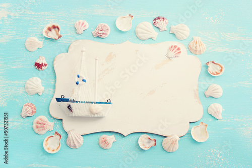 nautical concept with white sail boat, seashells and blank board for copy space over blue wooden background