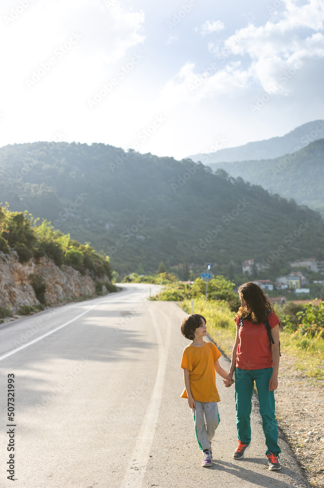 A boy and his mother are walking along the road against the backdrop of mountains