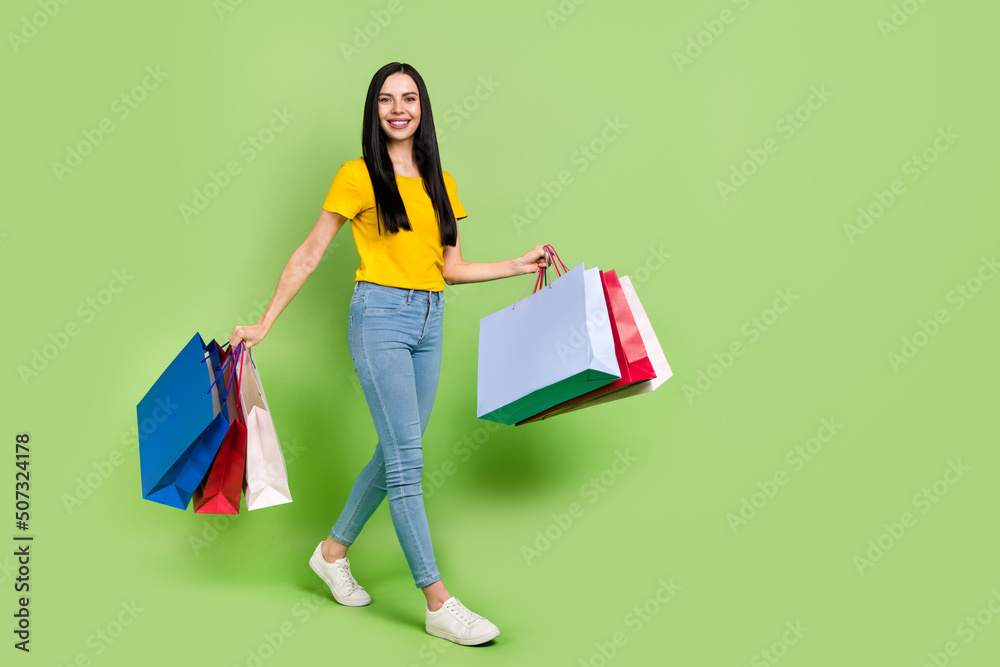 Full size profile photo of charming positive girl hold packages walking isolated on green color background Full size profile photo of charming positive girl hold packages walking isolated on green color background