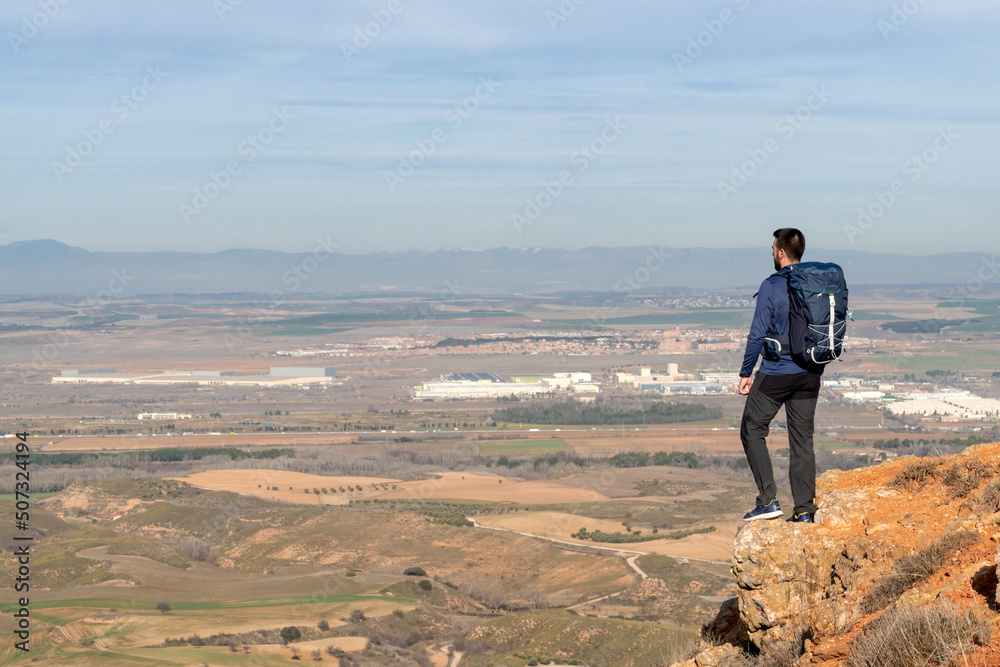 Young bearded man with a backpack looking down at the city from the top of the mountain Young bearded man with a backpack looking down at the city from the top of the mountain