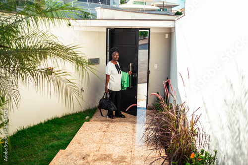 Mulher abrindo a porta de entrada da casa e segurando uma mala