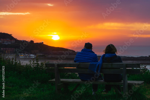 hombre y mujer, pareja contemplando un bonito uy colorido atardecer en la costa desde un banco