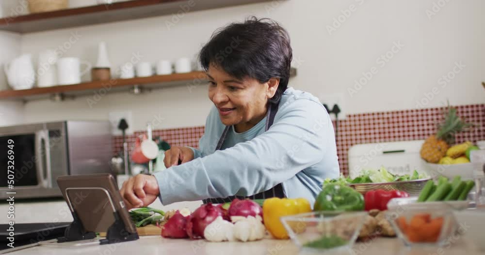 Asian senior woman using digital tablet while chopping vegetables in the kitchen at home Asian senior woman using digital tablet while chopping vegetables in the kitchen at home