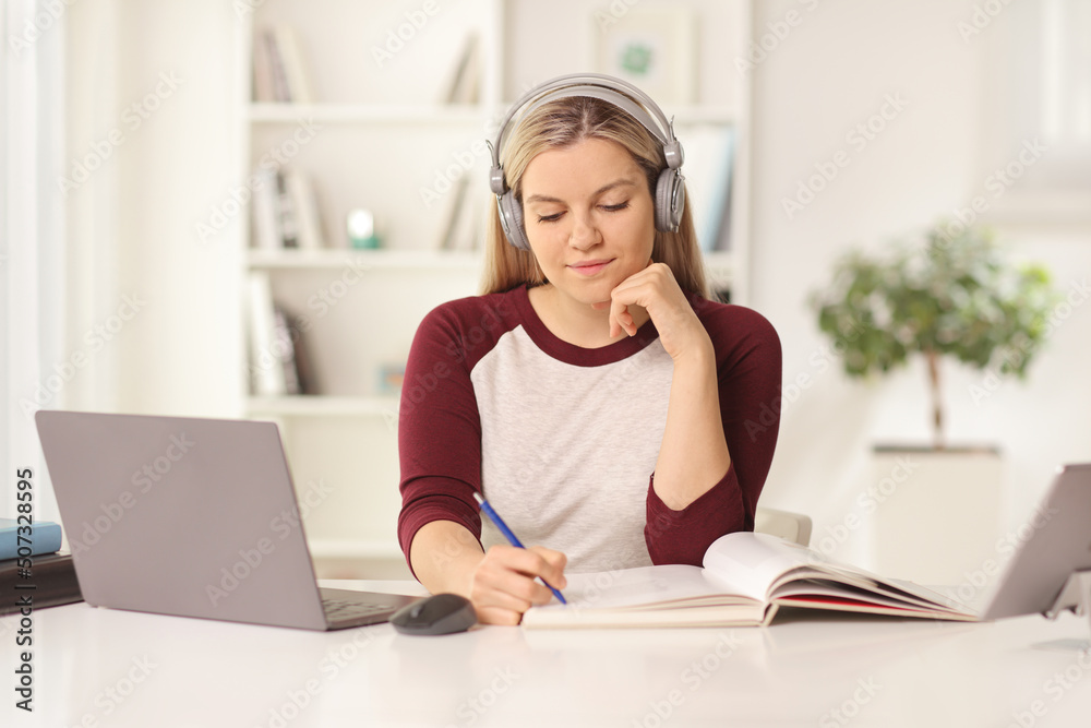 Female student sitting in front of a laptop computer at home with headphones Female student sitting in front of a laptop computer at home with headphones