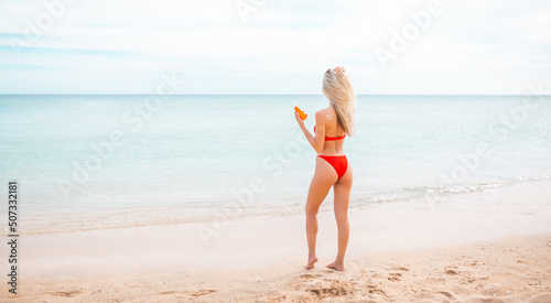 Woman applying sun cream on tanned body In form heart love to protect her skin. Girl using sunscreen. Female holding suntan lotion  moisturizing sunblock on sunny day with blurry sea in the background