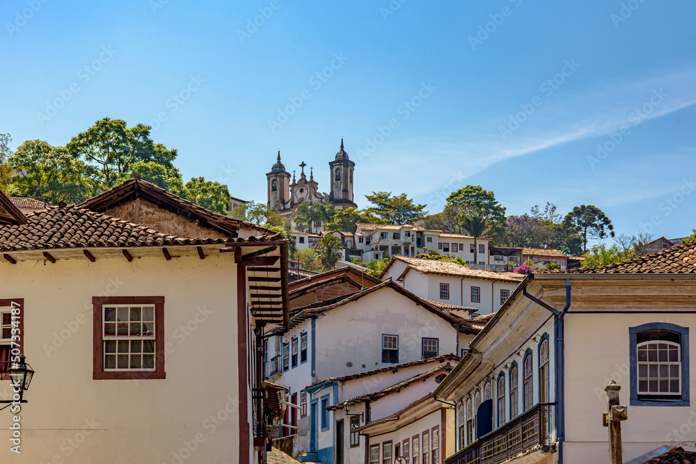 Facade of colonial-style houses in the historic city of Ouro Preto in Minas Gerais with a baroque church on top of the hill in the background.