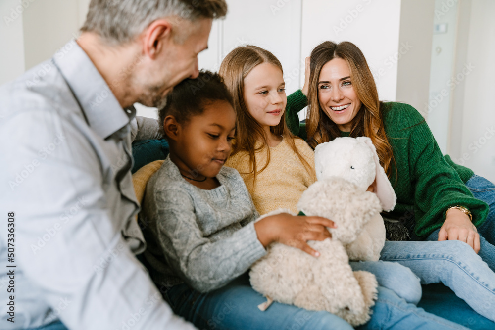 Happy family sitting on couch, adopted sisters playing stuffed toys Happy family sitting on couch, adopted sisters playing stuffed toys