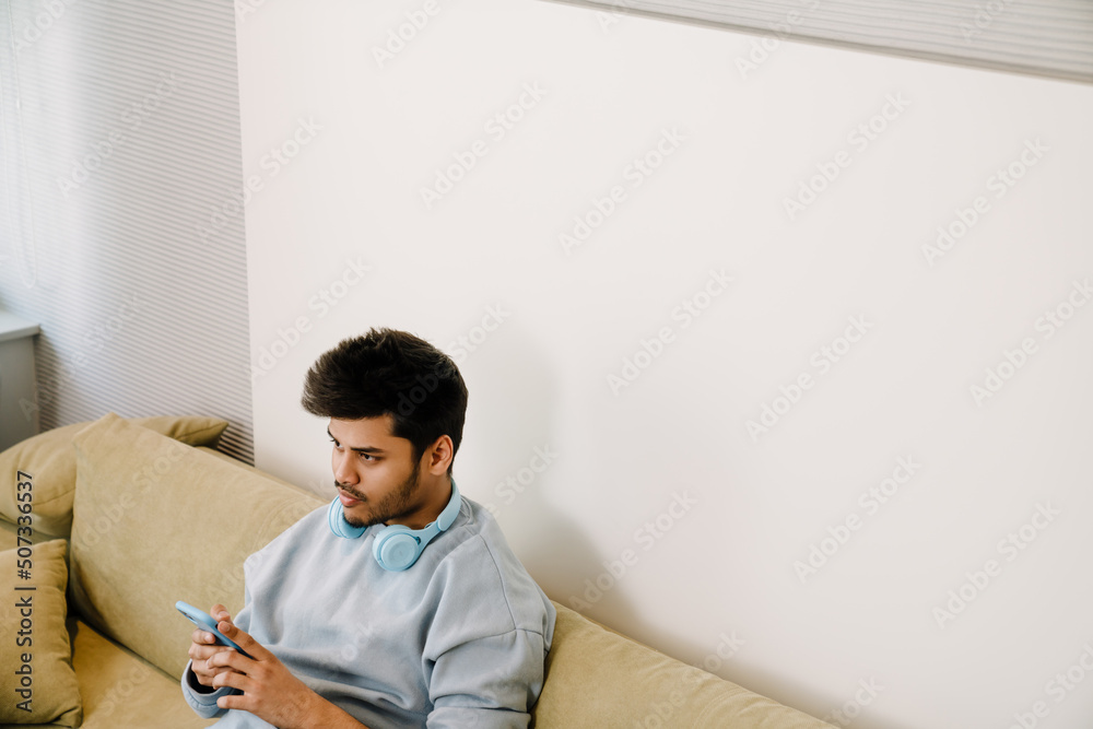 Fototapeta premium Young indian boring man with headphones on his neck