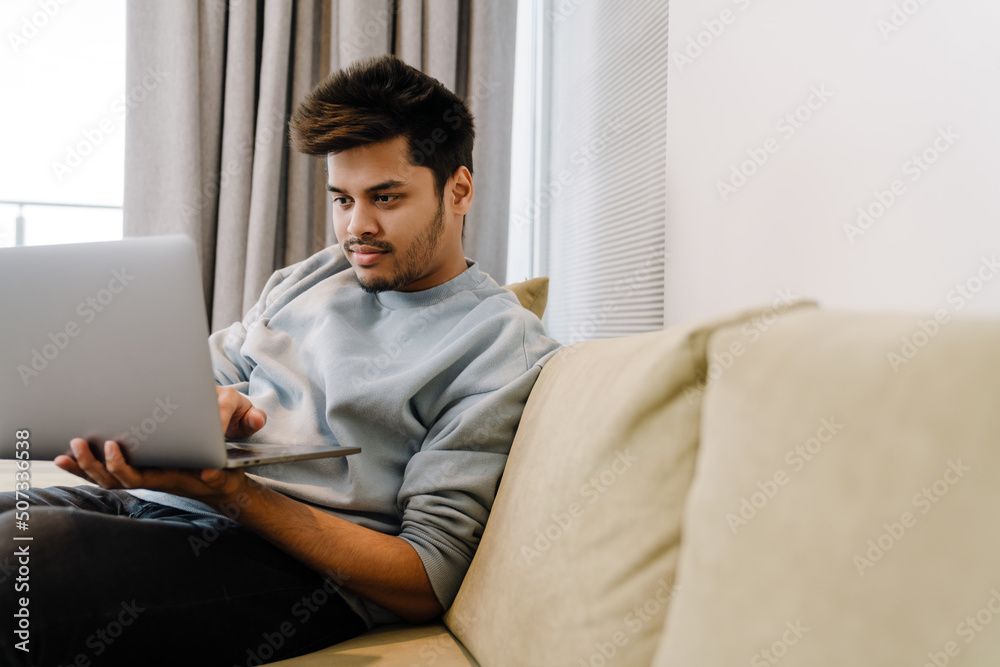 Young indian man workong with laptop sitting on sofa Young indian man workong with laptop sitting on sofa