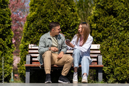 Happy couple watching a smart phone sitting on a bench in a park