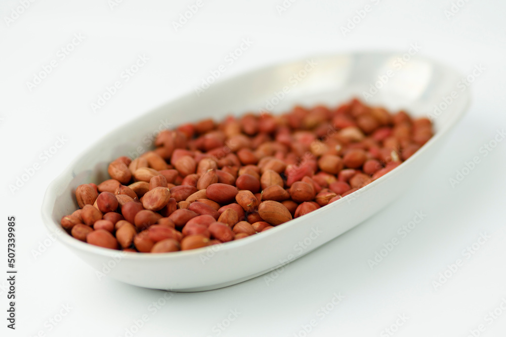 Unpeeled peanuts in a plate on a white background. Unpeeled peanuts in a plate on a white background.
