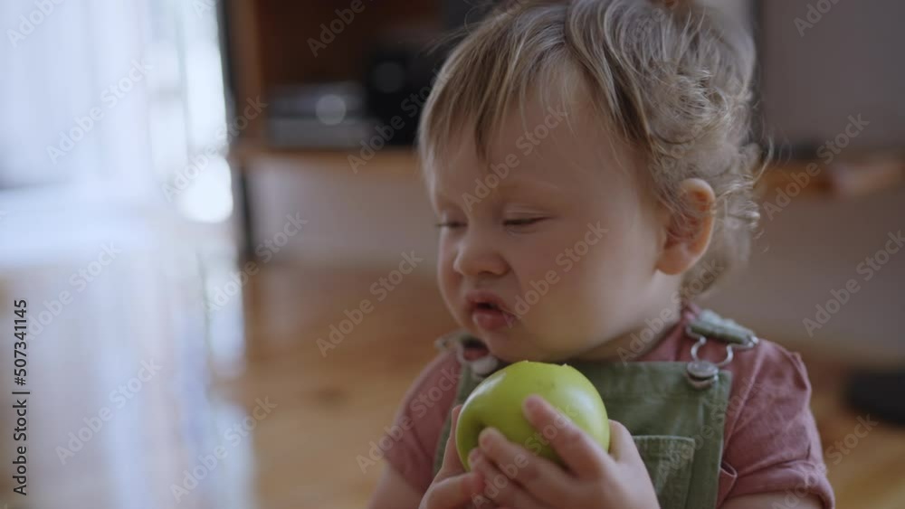 Cinematic shot of happy smiling cute curious little toddler boy eating fresh biologic apple full of vitamins while his mother is caressing he with affection in kitchen at home with sun shining light. Cinematic shot of happy smiling cute curious little toddler boy eating fresh biologic apple full of vitamins while his mother is caressing he with affection in kitchen at home with sun shining light.