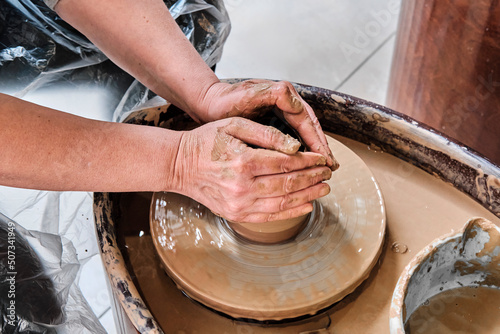 Hands of older woman sculpting clay vase on potter's wheel.