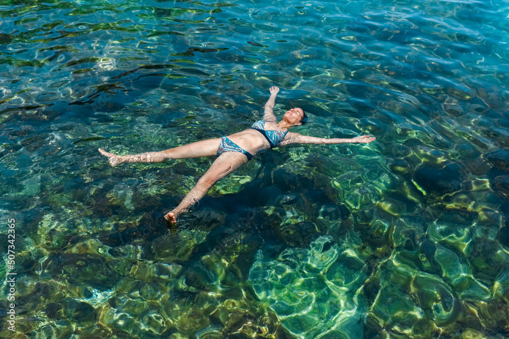 Young woman enjoys floating in a rocky tide pool in Tenerife, Canary Islands. The place is a puddle next to the sea called Charco de la Laja. 