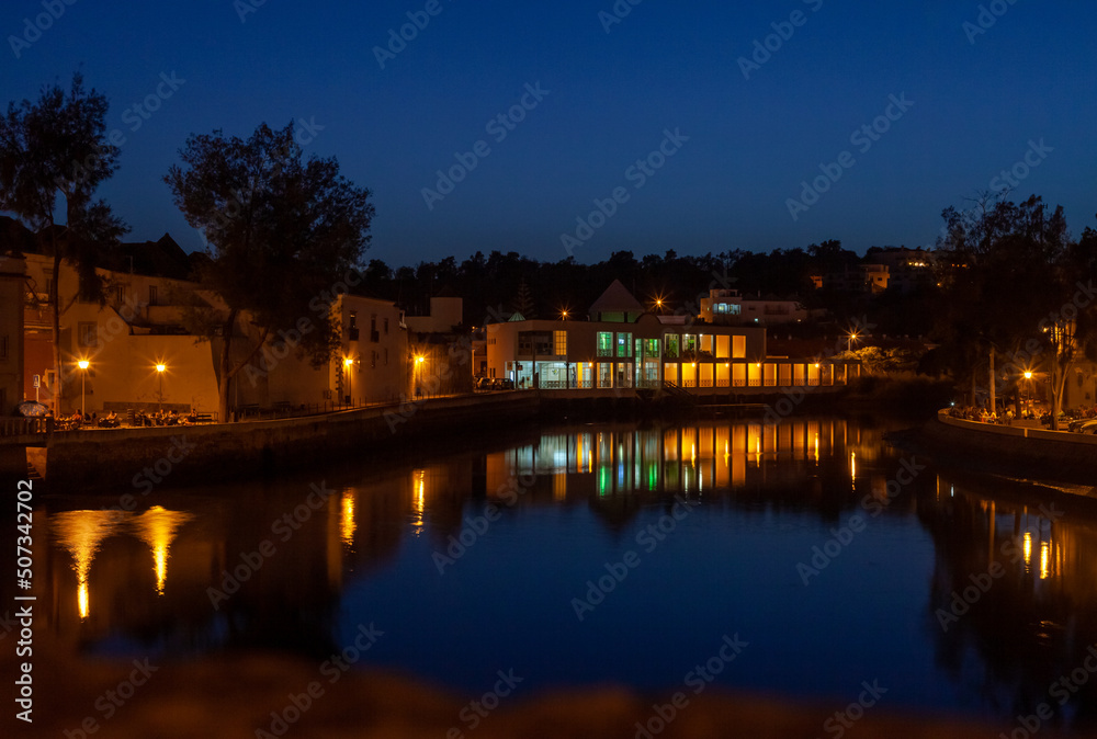 Naklejka premium illuminated houses by a river at dusk in the Portuguese town of Tavira