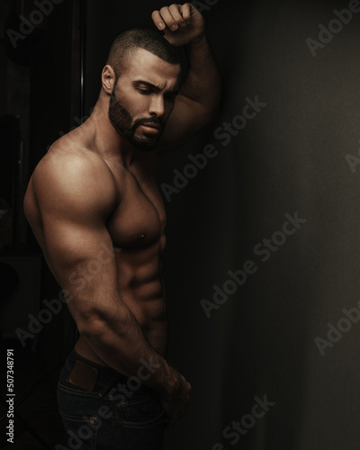 Dark portrait of shirtless bearded fitness man in jeans
