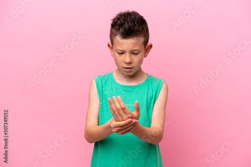 Little caucasian boy isolated on pink background suffering from pain in hands