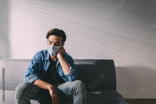 An upset health problem Asian patient man wearing a face mask at home or hospital alone sad and waiting for a doctor. Hospital and Health care during Coronavirus or Covid-19 quarantine concept