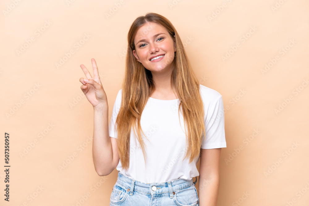 Young caucasian woman isolated on beige background smiling and showing victory sign