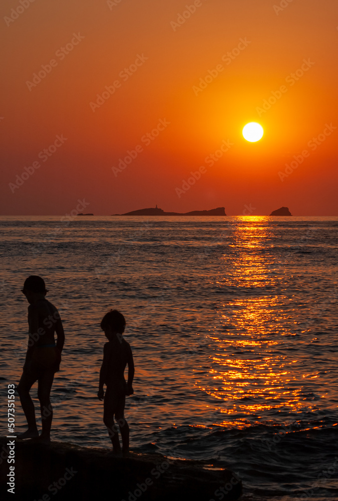 a couple of children playing on a beach at sunset
