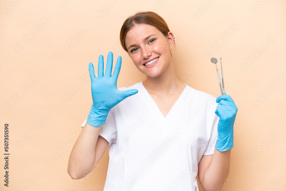 Dentist caucasian woman holding tools isolated on beige background counting five with fingers Dentist caucasian woman holding tools isolated on beige background counting five with fingers