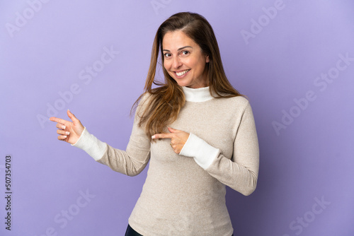 Middle age Brazilian woman isolated on purple background surprised and pointing side