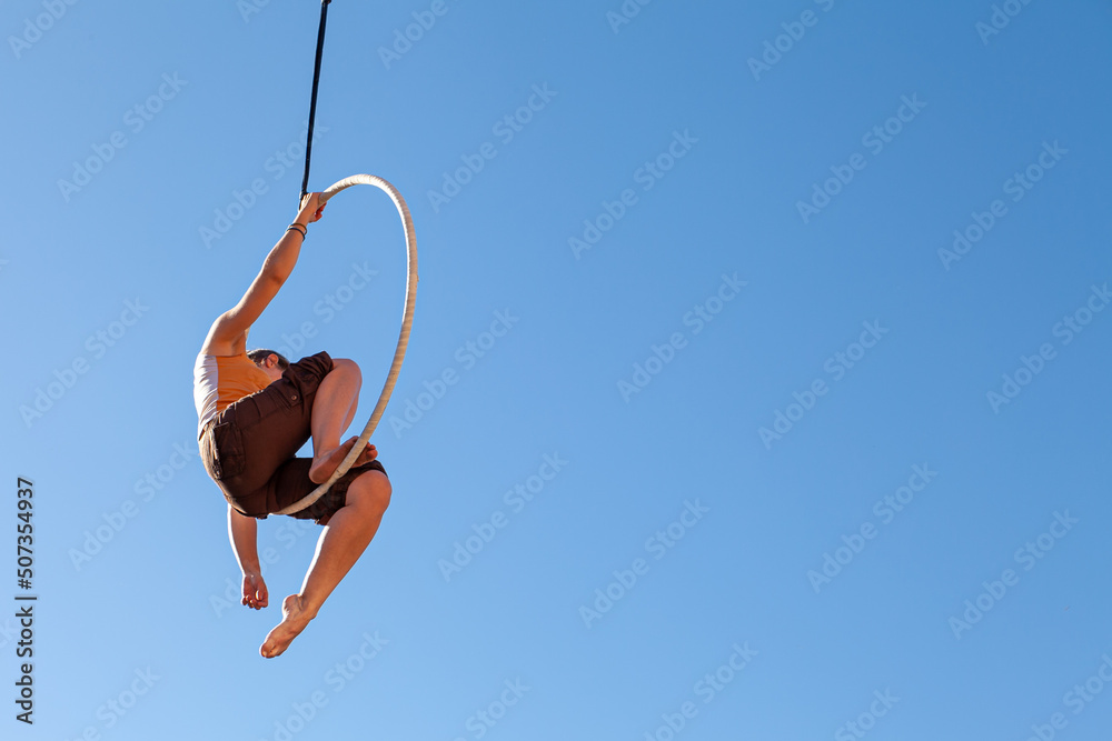a young trapeze artist suspended in mid-air attached to a circus hoop
