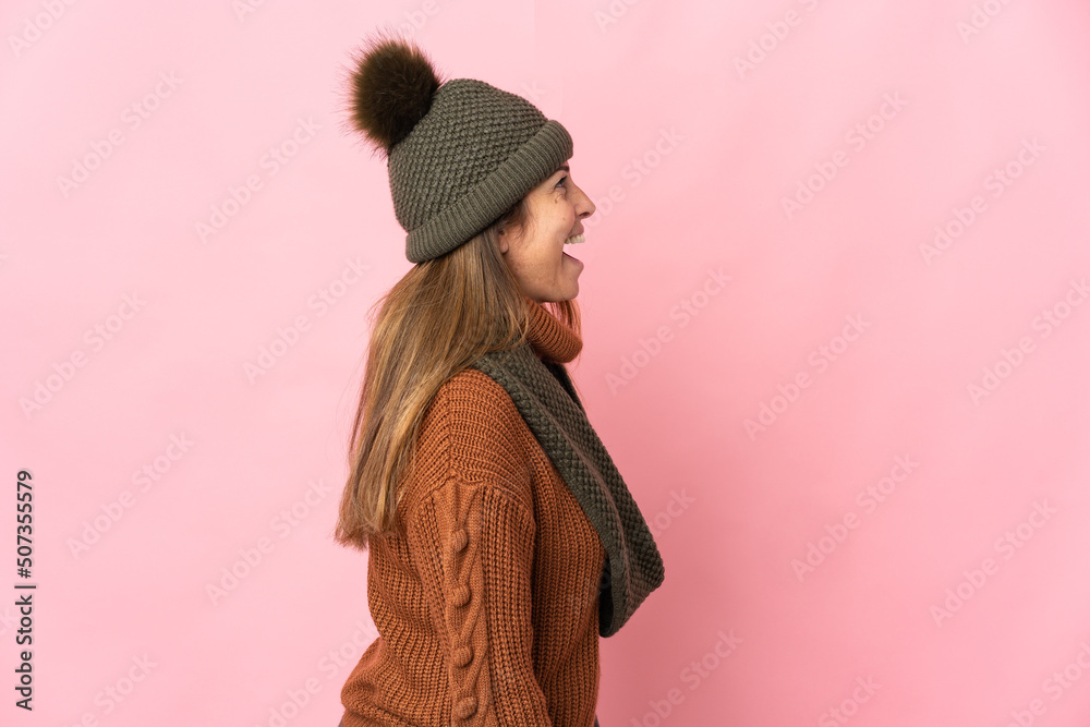 Middle age woman with winter hat isolated on pink background laughing in lateral position Middle age woman with winter hat isolated on pink background laughing in lateral position