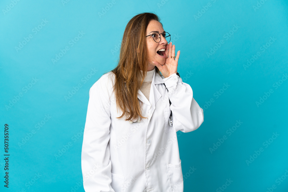 Middle age Brazilian doctor woman isolated on blue background shouting with mouth wide open to the side Middle age Brazilian doctor woman isolated on blue background shouting with mouth wide open to the side