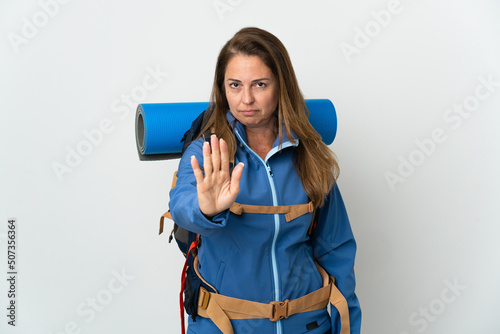 Middle age mountaineer woman with a big backpack over isolated background making stop gesture