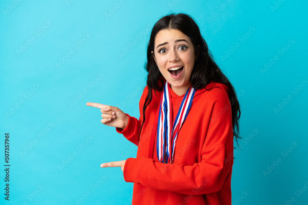 Young woman with medals isolated on white background surprised and pointing side Young woman with medals isolated on white background surprised and pointing side