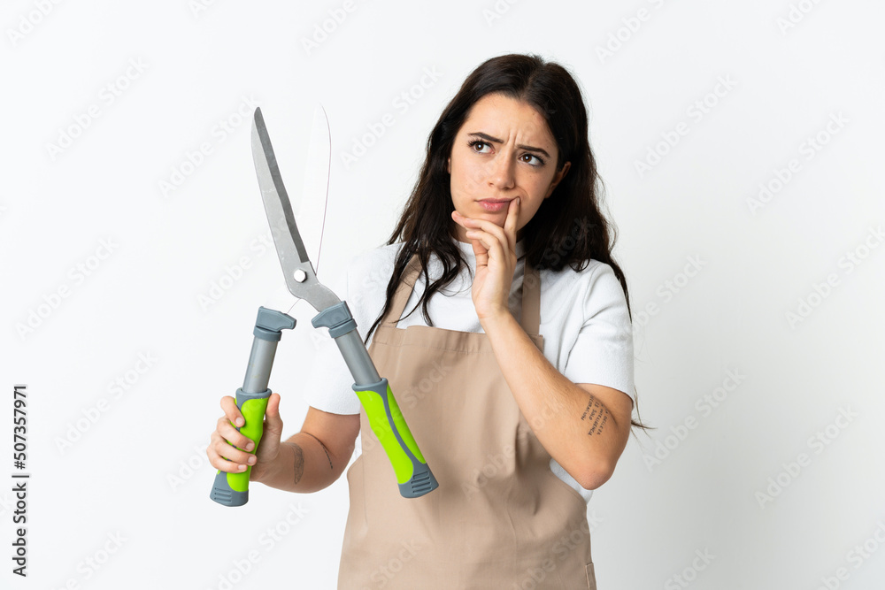 Young caucasian woman holding a plant isolated on white background having doubts while looking up