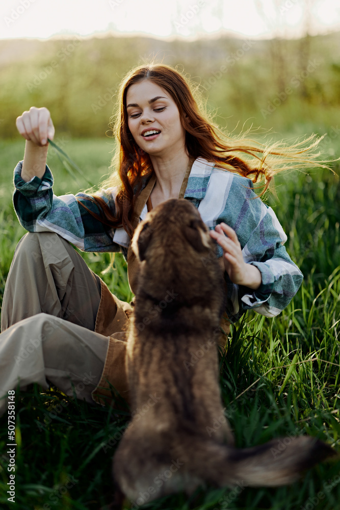 Happy woman sitting in nature and playing with her pet in the park sitting on the green grass Happy woman sitting in nature and playing with her pet in the park sitting on the green grass