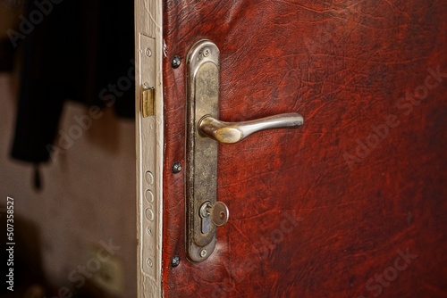 gray metal door handle and door lock with a key in the door on red leather in the room