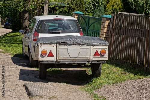 a car with a gray trailer covered with a black tarpaulin stands on the street near the fence