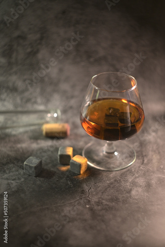 transparent whiskey with a bottle and a wooden cork on a dark background. whiskey stones in a glass