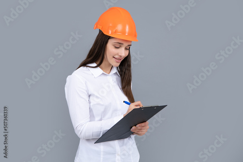 Business builder woman with clipboard, portrait on gray. Portrait of female worker in hardhat helmet.
