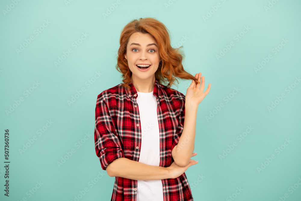 amazed redhead girl in checkered shirt on blue background