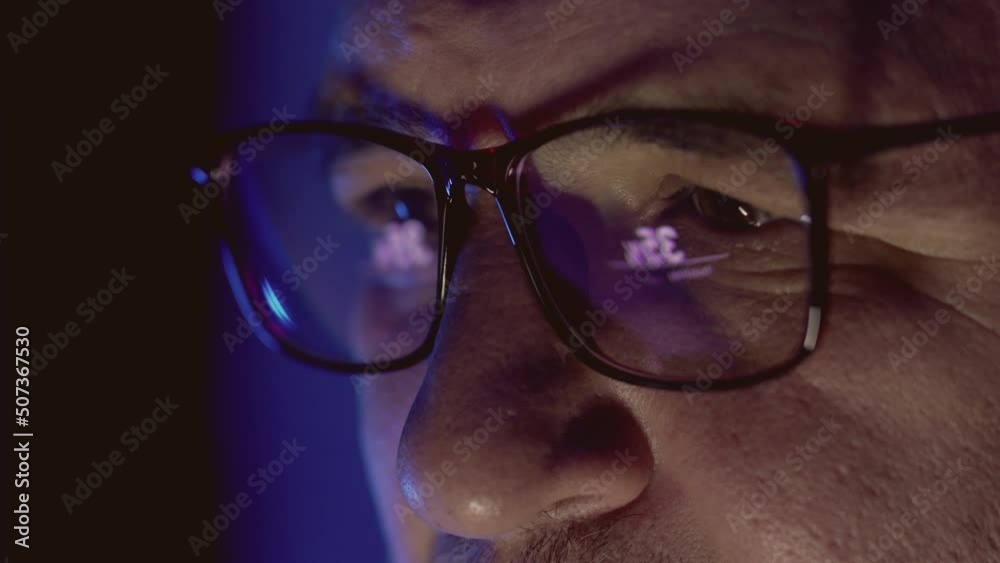 Close-up. The eyes of a man wearing glasses, who is carefully looking at the monitor or working devices. The glasses reflect information. Small focus. Close-up. The eyes of a man wearing glasses, who is carefully looking at the monitor or working devices. The glasses reflect information. Small focus.