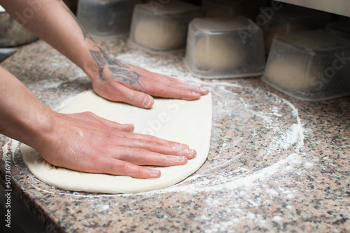 Close-up of male hands baker kneads raw pizza dough. Fast food. Pizza delivery.