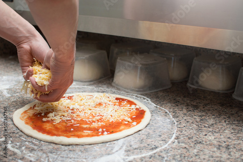 Cook in the kitchen putting the ingredients on the pizza. Pizza concept.