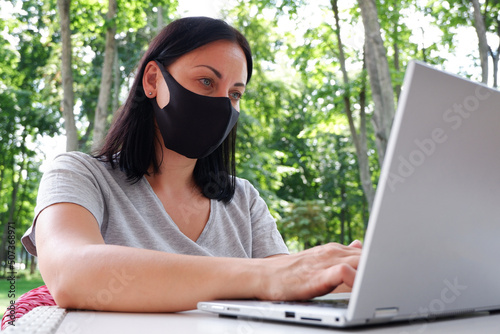 A girl in a medical mask makes a video conference through a laptop and sits outside in a cafe. Distance learning online education and work. Coronavirus Pandemic Quarantine