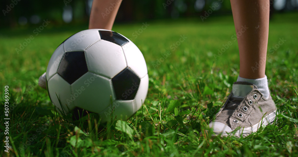 Unknown kids feet playing football on grass close up. Boy legs kick ball in park