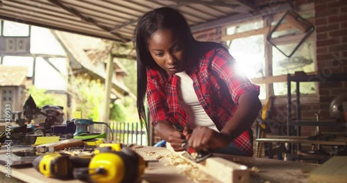 African American female carpenter working on a wooden board in a studio by hand