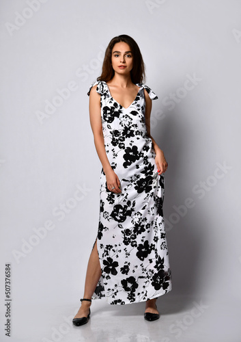Luxurious young slender girl with long hair in a long dress with a black and white floral print. Getting ready for a date on a warm summer evening.