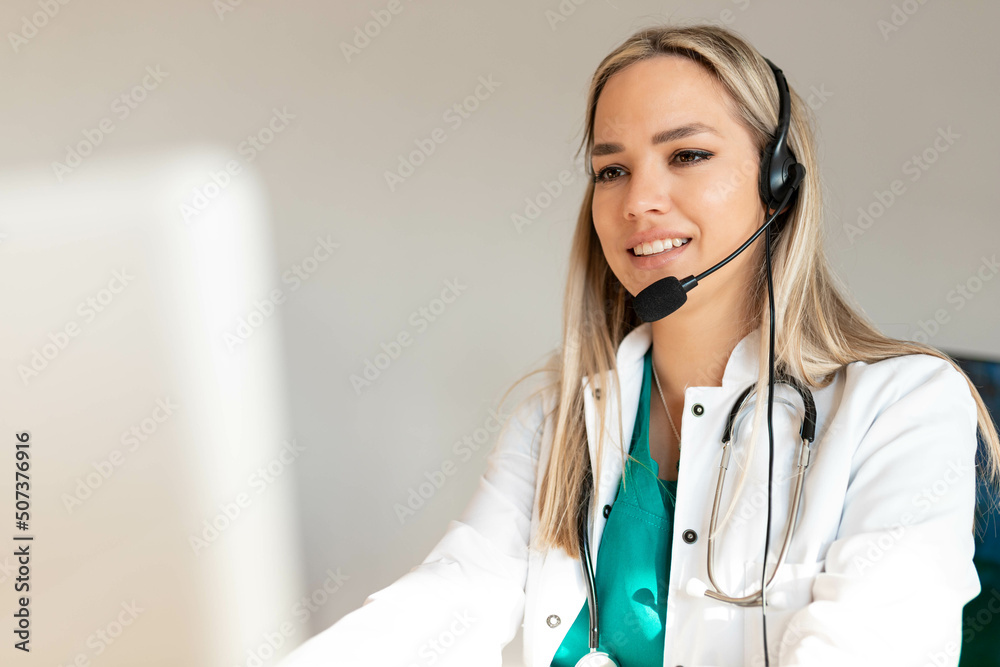 Smiling Attractive Young Woman Wearing Headset and stethoscope Near Her Computer Monitor. Health care customer support concept or ambulance dispatcher. Smiling Attractive Young Woman Wearing Headset and stethoscope Near Her Computer Monitor. Health care customer support concept or ambulance dispatcher.