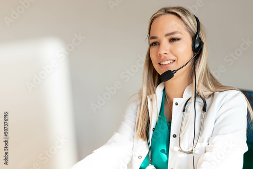 Smiling Attractive Young Woman Wearing Headset and stethoscope Near Her Computer Monitor. Health care customer support concept or ambulance dispatcher. 