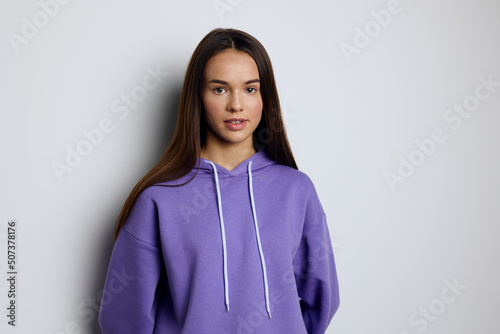 a calm, peaceful woman stands against a white background in a purple tracksuit with her hands down in a relaxed manner © Tatiana