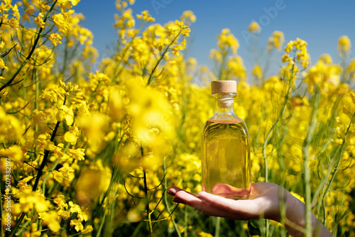 Rapeseed oil in a transparent glass bottle in hand on a background of rapeseed field